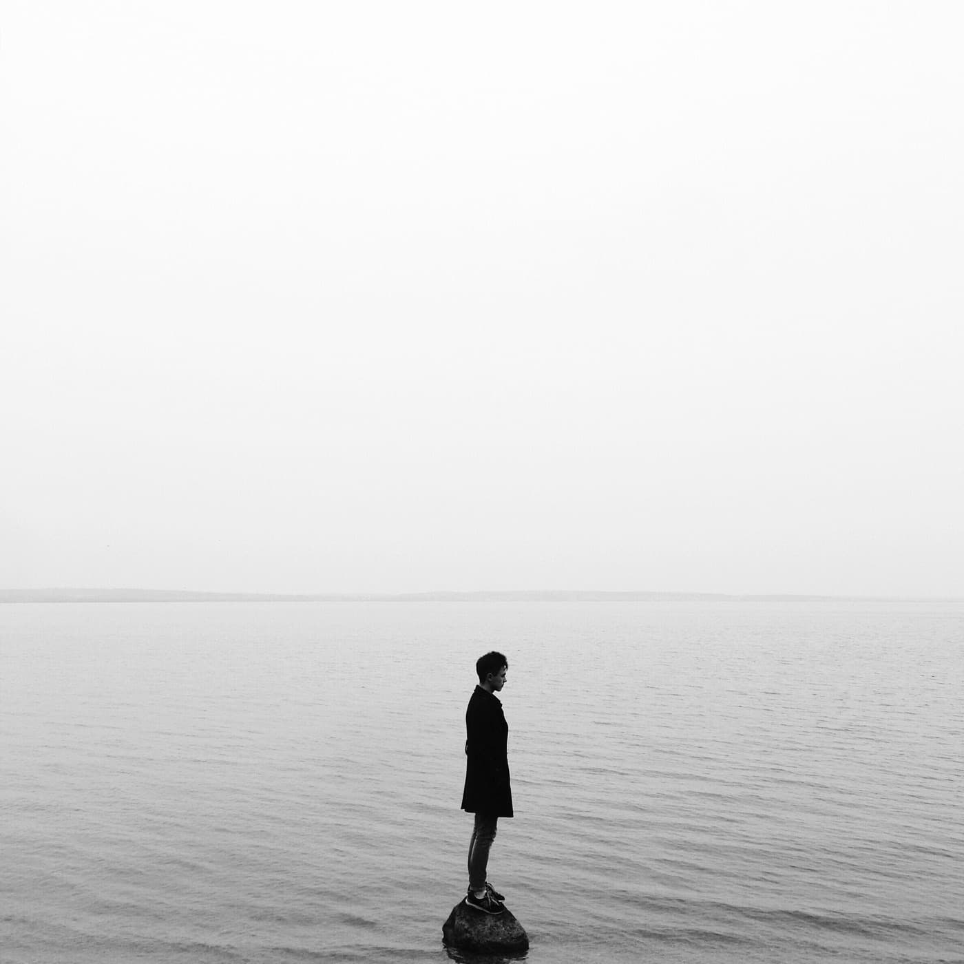 A person standing alone on a rock beside calm water