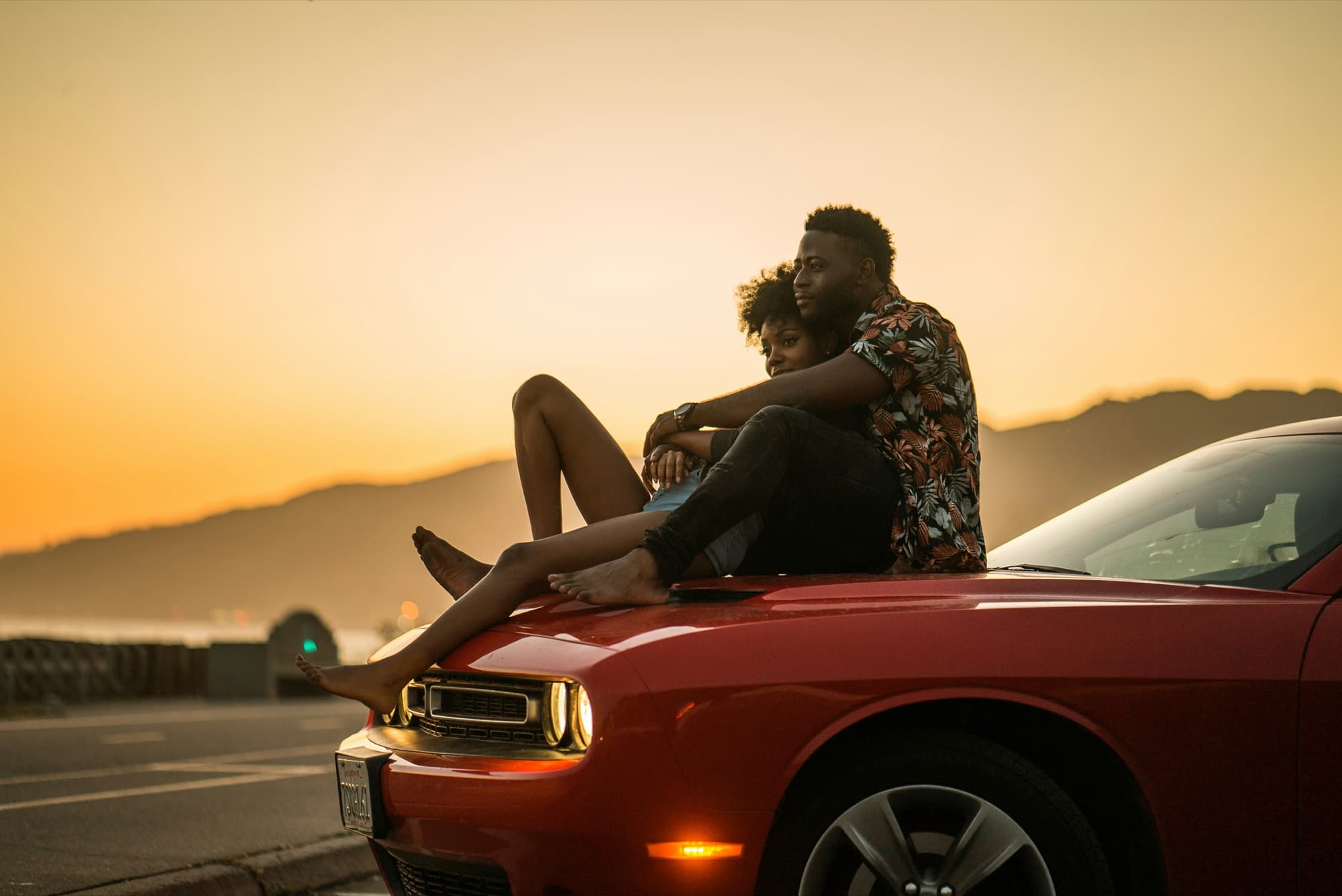 Couple sitting closely together on a red car at sunset